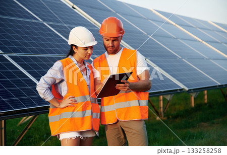 Reading the information from notepad. Man and woman, workers are near solar panels, in uniform Reading the information from notepad. Man and woman, workers are near solar panels, in uniform 133258258