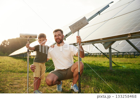 Time to clean the surface. Father with his little son are together near the solar panels Time to clean the surface. Father with his little son are together near the solar panels 133258468