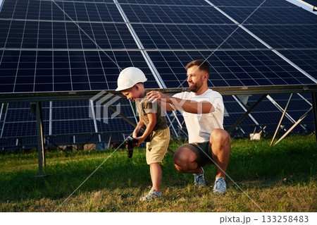 In hard hat and with drill. Father with his little son are together near the solar panels 133258483