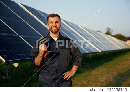 Outside, standing and holding the drill. Man is working with solar panels outdoors at daytime 133258546