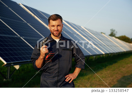 Outside, standing and holding the drill. Man is working with solar panels outdoors at daytime Outside, standing and holding the drill. Man is working with solar panels outdoors at daytime 133258547