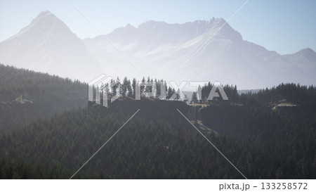 Higher peaks tower over lush forests, bathed in soft morning light. The tranquil scene captures natures beauty, inviting exploration and reflection amidst the grandeur of the wilderness. 133258572