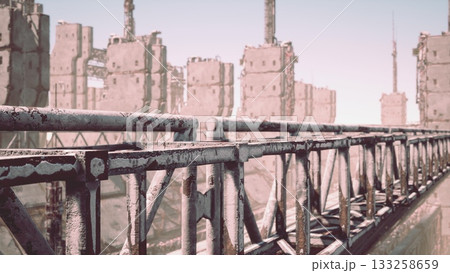 A rugged walkway spans an industrial area filled with towering structures, showcasing a blend of resilience and decay under a bright sky, hinting at a forgotten era of innovation. 133258659
