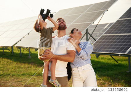 Looking through the binoculars. Father, mother and little son are outdoors near solar panels 133258692