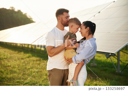Embracing each other. Father, mother and little son are outdoors near solar panels Embracing each other. Father, mother and little son are outdoors near solar panels 133258697