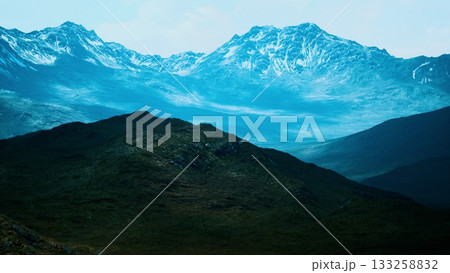 Snow capped mountains rise majestically against a clear sky. Valleys stretch below, showcasing natural beauty and tranquility in a remote wilderness, untouched by human presence. 133258832