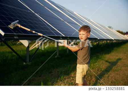 Busy by cleaning the surface. Little boy is with solar panels outdoors Busy by cleaning the surface. Little boy is with solar panels outdoors 133258881
