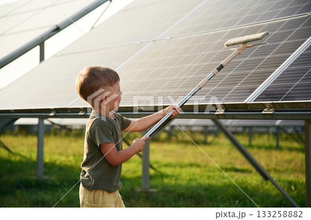 Busy by cleaning the surface. Little boy is with solar panels outdoors 133258882