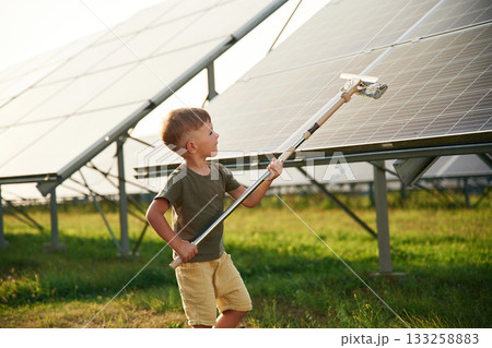 Busy by cleaning the surface. Little boy is with solar panels outdoors 133258883