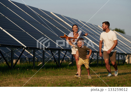 Active, running with toy plane. Father, mother and little son are outdoors near solar panels Active, running with toy plane. Father, mother and little son are outdoors near solar panels 133259012