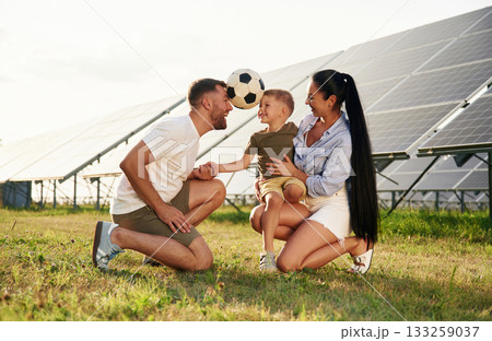 Rural scene, with soccer ball. Father, mother and little son are outdoors near solar panels 133259037