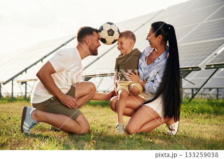 Rural scene, with soccer ball. Father, mother and little son are outdoors near solar panels 133259038