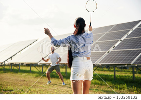 Playing badminton. Couple are having fun near the solar panels outdoors Playing badminton. Couple are having fun near the solar panels outdoors 133259132