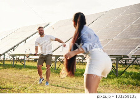 Badminton game. Couple are having fun near the solar panels outdoors Badminton game. Couple are having fun near the solar panels outdoors 133259135