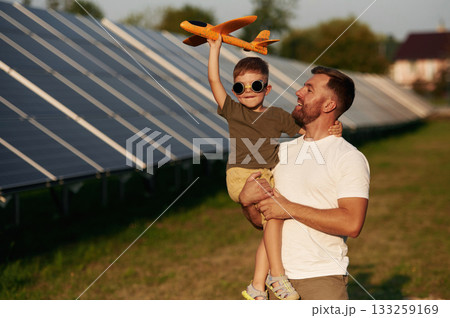 Aviator glasses and toy plane. Father with his little son are together near the solar panels Aviator glasses and toy plane. Father with his little son are together near the solar panels 133259169