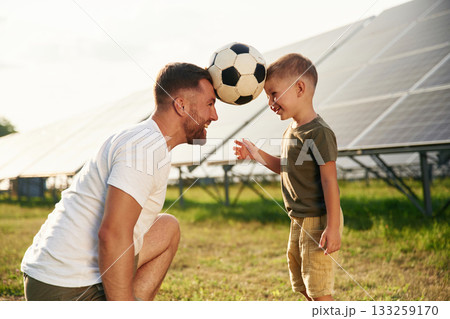 Soccer ball on heads. Father with his little son are together near the solar panels Soccer ball on heads. Father with his little son are together near the solar panels 133259170