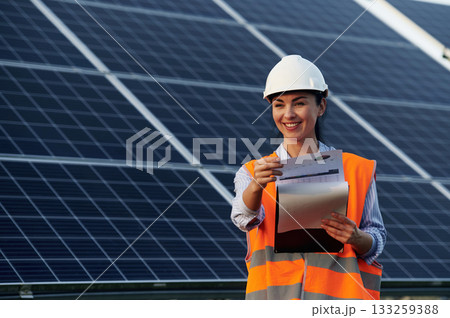 Checking the data, with notepad. Female worker engineer in uniform is near solar panels Checking the data, with notepad. Female worker engineer in uniform is near solar panels 133259388