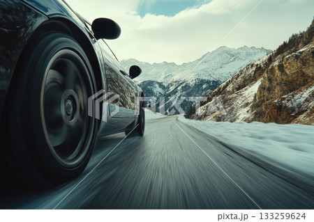 Sleek Sports Car Driving on a Snowy Mountain Road with Scenic Landscape Views in Winter 133259624