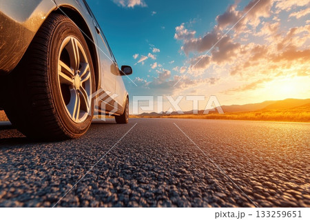 Close-Up View of Car Tire on Open Road Under Stunning Sunset Sky with Dramatic Clouds 133259651