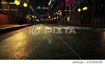 A quiet street in the heart of the city features shimmering reflections on wet pavement. Colorful lights from nearby buildings create an inviting atmosphere under the night sky. 133260299