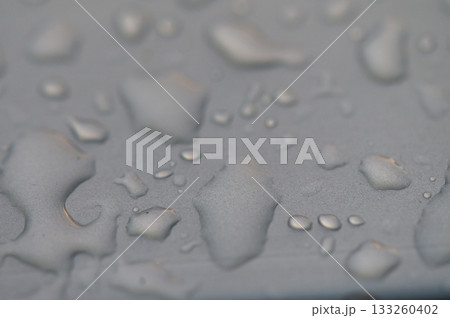 Water droplets glisten on a smooth surface reflecting soft light at dusk near a serene body of water 133260402