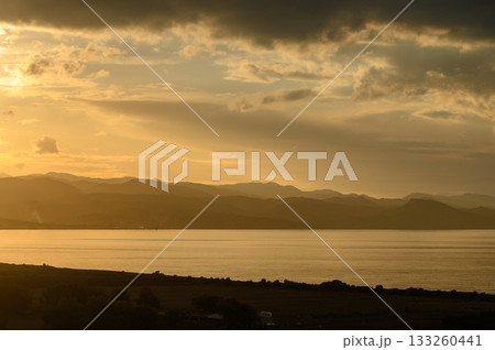Golden sunset illuminates tranquil waters reflecting distant mountain silhouettes Golden sunset illuminates tranquil waters reflecting distant mountain silhouettes 133260441