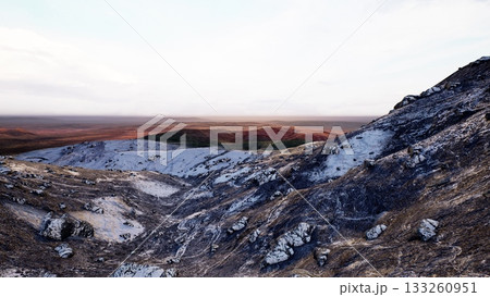 Breathtaking hills rise dramatically, showcasing dark rocks and a soft glow from the setting sun. 133260951