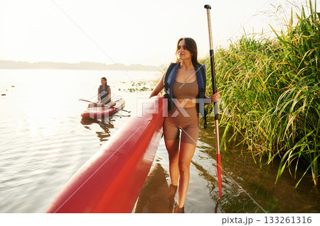 Walking to the shore. Women friends are on sup board on the lake together Walking to the shore. Women friends are on sup board on the lake together 133261316