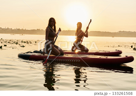 Against sunset light. Women friends are on sup board on the lake together 133261508