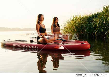 In lotus pose. Women friends are on sup board on the lake together 133261522