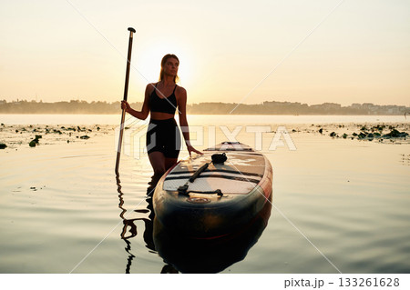 Calm and peaceful, standing and posing. Young woman is with the sup board on the lake 133261628