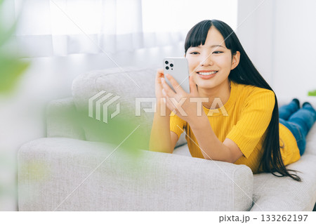 ソファに寝転がってスマホを使う女性　 133262197