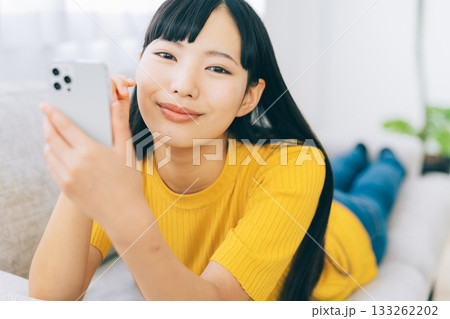 ソファに寝転がってスマホを使う女性　 133262202