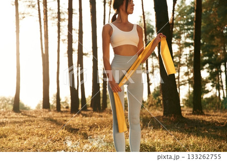 Holding yellow stretching band. Woman is doing yoga fitness exercises in the forest Holding yellow stretching band. Woman is doing yoga fitness exercises in the forest 133262755