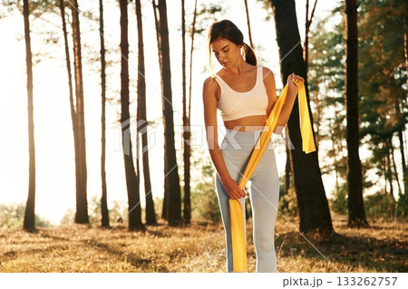Holding yellow stretching band. Woman is doing yoga fitness exercises in the forest Holding yellow stretching band. Woman is doing yoga fitness exercises in the forest 133262757