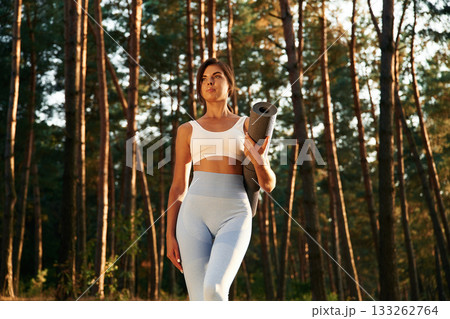 Mat in hand, standing. Woman is doing yoga fitness exercises in the forest 133262764