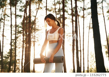 Bright sunlight, holding mat. Woman is doing yoga fitness exercises in the forest Bright sunlight, holding mat. Woman is doing yoga fitness exercises in the forest 133262773