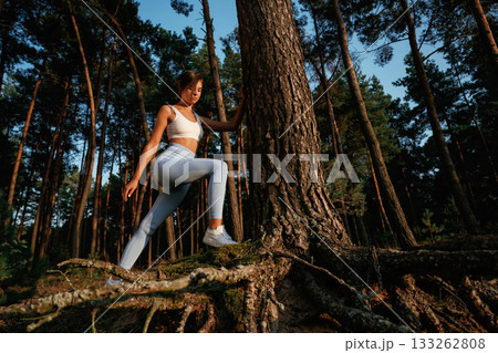 Exploring new places. Woman in fitness clothes is in the forest near the tree Exploring new places. Woman in fitness clothes is in the forest near the tree 133262808