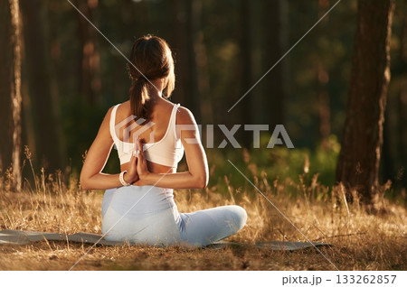 Sitting in lotus pose. Woman is doing yoga fitness exercises in the forest Sitting in lotus pose. Woman is doing yoga fitness exercises in the forest 133262857