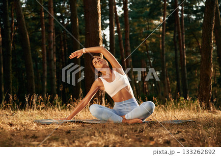 Many of the trees at background, sitting. Woman is doing yoga fitness exercises in the forest 133262892
