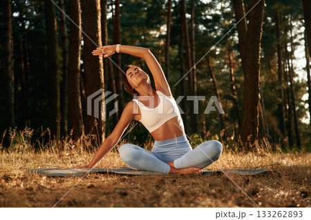Many of the trees at background, sitting. Woman is doing yoga fitness exercises in the forest Many of the trees at background, sitting. Woman is doing yoga fitness exercises in the forest 133262893