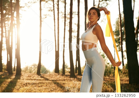 Yellow stretching band in hands. Woman is doing yoga fitness exercises in the forest Yellow stretching band in hands. Woman is doing yoga fitness exercises in the forest 133262950