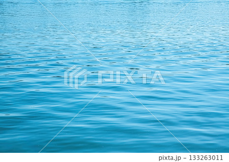 Calm river surface displaying gentle ripples and seamless blue hues under soft sunlight Calm river surface displaying gentle ripples and seamless blue hues under soft sunlight 133263011