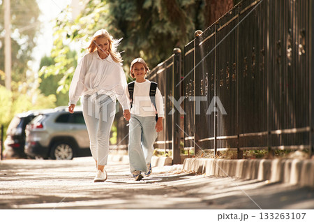 Front view, walking. Schoolgirl with her mother are outdoors together 133263107