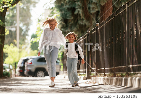 Front view, walking. Schoolgirl with her mother are outdoors together 133263108