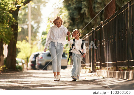 Front view, walking. Schoolgirl with her mother are outdoors together 133263109