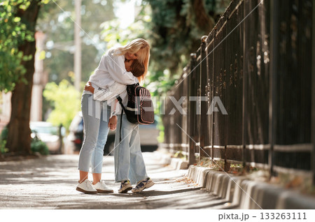 Embracing each other. Schoolgirl with her mother are outdoors together 133263111