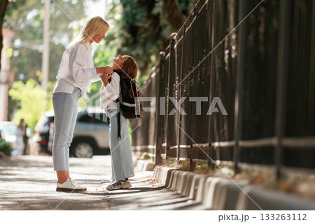 Woman is supporting daughter. Schoolgirl with her mother are outdoors together 133263112