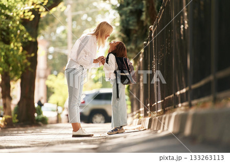 Woman is supporting daughter. Schoolgirl with her mother are outdoors together 133263113