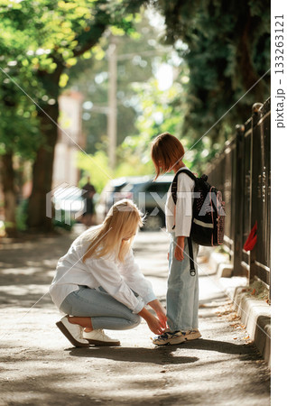 Side view. Schoolgirl with her mother are outdoors together Side view. Schoolgirl with her mother are outdoors together 133263121